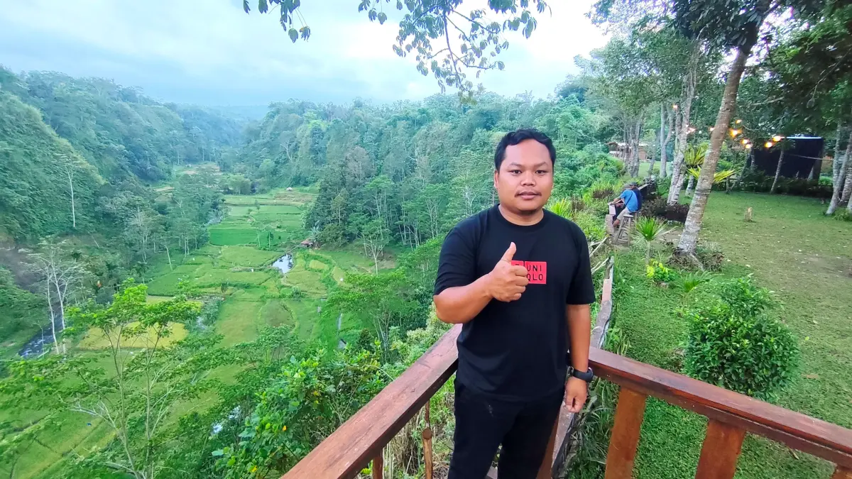 Rohim pemilik Camping Ground Lembah Datu berfoto dengan latar pemandangan sawah dan kawasan hutan nan sejuk, di Dusun Gelogor, Desa Pemepek, Pringgarata, Loteng. (Dewi/Lombok Post) 