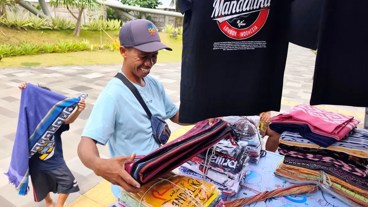 Lalu Mian sedang merapikan aneka kain dan pakaian ikonik Mandalika di depan Sirkuit Internasional Pertamina Mandalika, Desa Kuta, Pujut, Loteng, Jumat (22/5). (Dewi/Lombok Post) 
