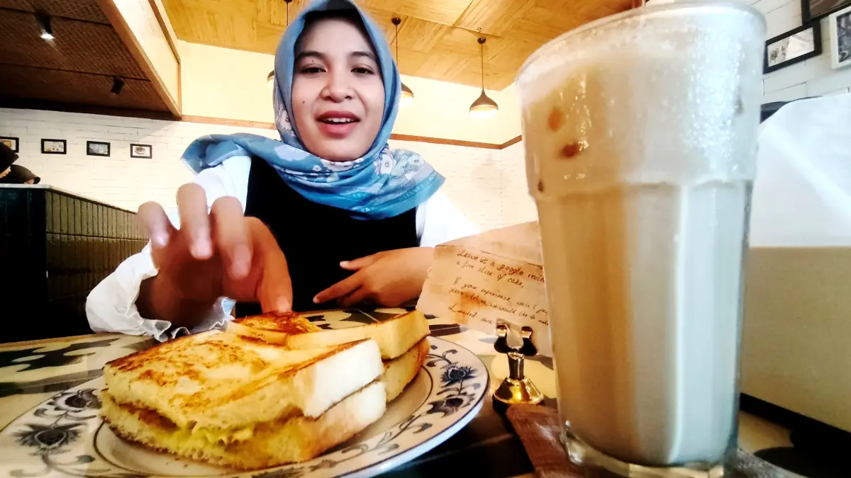 Seorang pengunjung menikmati segelas Ice Kopi Tarik dan Roti Bakar Sangkaya yang menjadi salah satu menu andalan di Kawan KopiTiam, The Mandalika, Kuta, Pujut, Loteng, belum lama ini. (Dewi/Lombok Post) 
