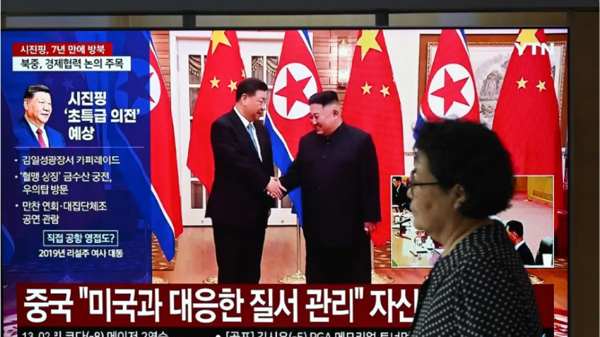 JALIN PERSAHABATAN: Seorang wanita melewati layar televisi yang menampilkan siaran berita pertemuan antara Presiden Tiongkok Xi Jinping dan pemimpin Korea Utara Kim Jong Un, di Seoul, Korsel, Senin (8/6). (JUNG YEON-JE/AFP)