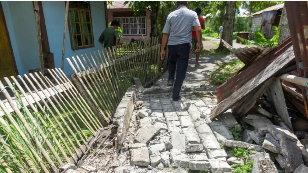 TERDAMPAK GEMPA: Warga Desa Peta Timur, Kabupaten Kepulauan Sangihe, Provinsi Sulawesi Utara melewati area perumahan yang rusak akibat terdampak gempa bumi berkekuatan magnitude 7,8 di lepas pantai selatan Filipina, Senin (8/6). (STENLY PONTOLAWOKANG / AFP)