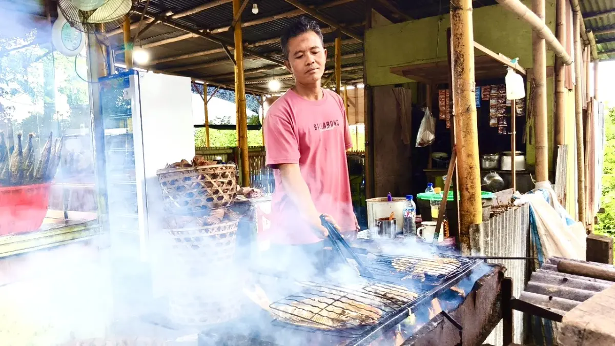 LAYANI PESANAN: Misbah yang tengah membakar ikan pesanan pembeli di lapak miliknya yang ada di pinggir jalan raya Taman Loang Baloq, Mataram. (Ferial/Lombok Post)