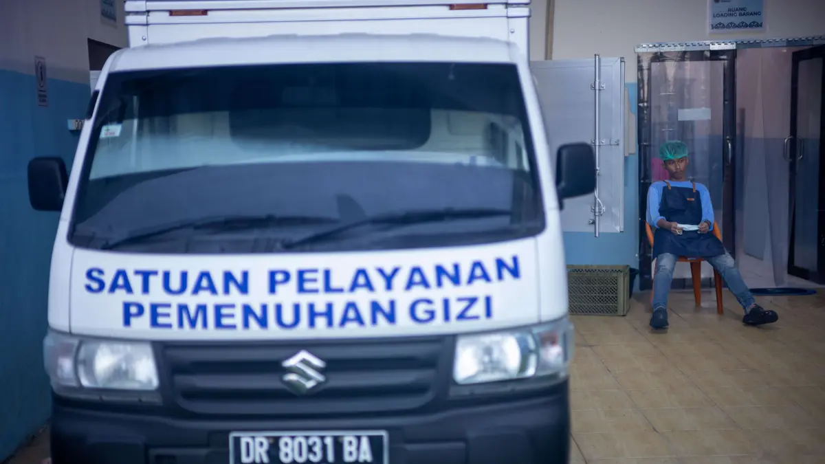 PROGRAM PUSAT: Seorang pegawai SPPG tampak bersantai di dekat kendaraan distribusi, menunggu proses penyaluran MBG ke sekolah-sekolah. (IVAN/LOMBOK POST)