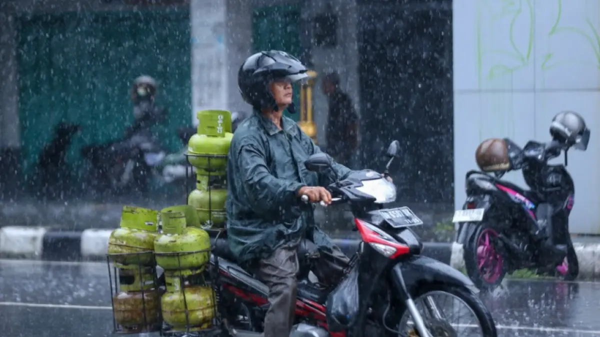 LANGKA DAN MAHAL: Seorang pria membawa tabung gas LPG 3 kg di bawah guyuran hujan saat melintas di kawasan Cakranegara, Kota Mataram. Pemerintah mewacanakan akan mengganti LPG 3 kg dengan kompor listrik. (IVAN/LOMBOK POST)