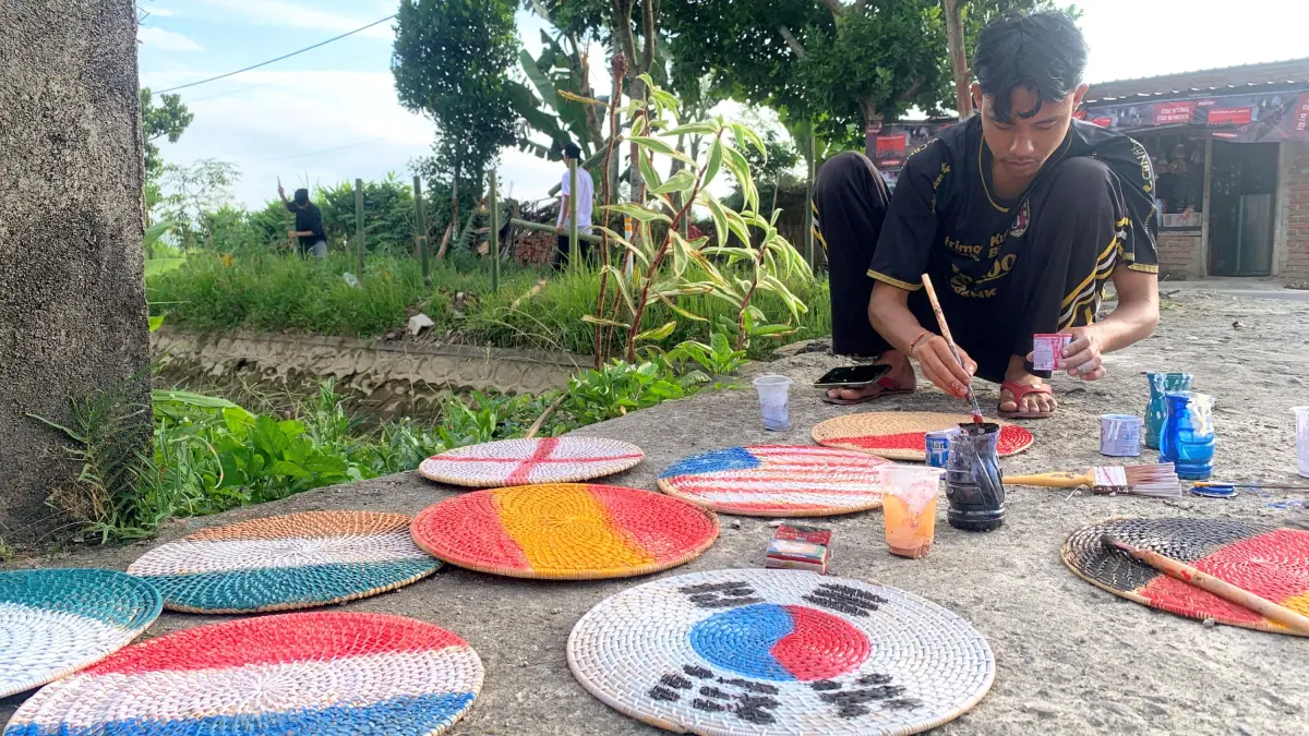 Pemuda Desa Pajangan, Kopang, Loteng mengecat lempengan anyaman ketak dengan warna-warna bendera negara peserta Piala Dunia 2026 di halaman kantor desa setempat, Selasa (16/6). (Dewi/Lombok Post) 