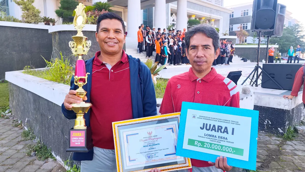 LOMBA DESA: Kepala Desa Bilebante Asrok Mudailun (kiri) menunjukkan piala dan hadiah uang tunai Juara I Lomba Desa Tingkat Kabupaten Lombok Tengah 2026, Jumat (19/6).  (Dewi/Lombok Post) 