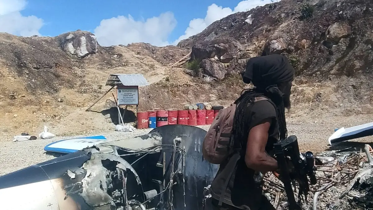 Salah seorang anggota OPM berpose dengan latar sisa-sisa  pesawat terbakar. Pesawat ini milik PT AMA dengan nomor registrasi PK-RCY yang terbakar di Bandara Ipdeheik, Balinggama, Yahukimo.