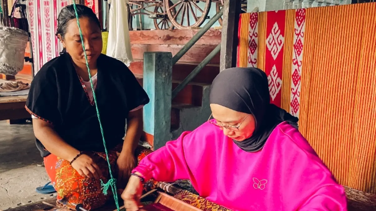 PENGALAMAN BERBEDA: Seorang wisatawan sedang mencoba menenun dan diajari langsung warga lokal saat berkunjung ke Desa Wisata Sukarara, Kecamatan Jonggat, Lombok Tengah. (Ivan/Lombok Post)