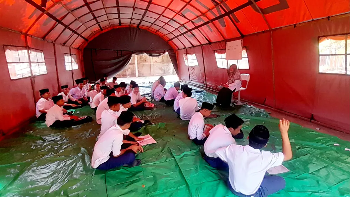 BERTAHAN DI TENDA DARURAT: Puluhan santri elas 9 MTs Nujumul Huda, Batu Samban, mengikuti proses kegiatan belajar mengajar (KBM) secara lesehan di dalam tenda darurat pascakebakaran yang menghanguskan empat ruang kelas mereka. (Foto: Toni/Lombok Post)