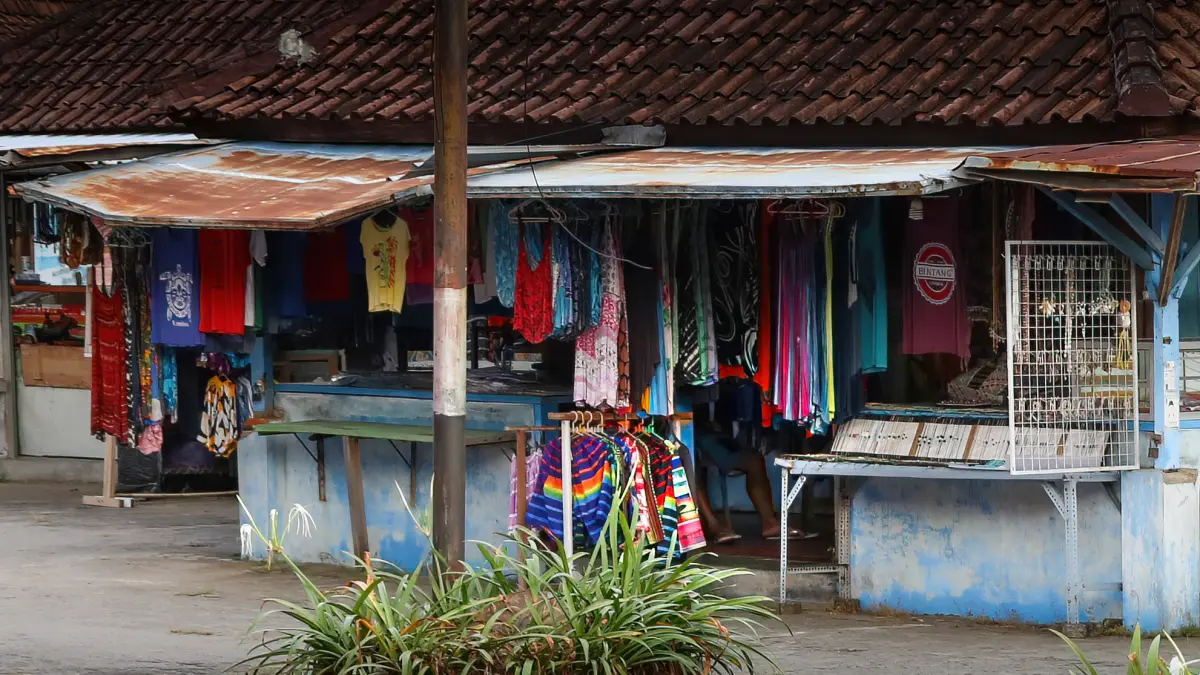 BUTUH PERBAIKAN: Seorang pedagang pakaian menunggu pembeli dari balik pakaian yang tergantung di Pasar Seni Senggigi, Lombok Barat, belum lama ini. (IVAN/LOMBOK POST)