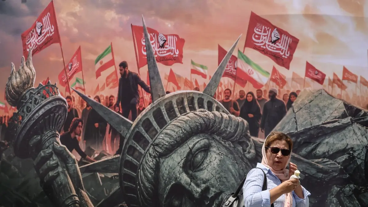 An Iranian woman walks past an anti-US billboard at Enghelab Square in central Tehran on August 3, 2026. Iran denied any negotiations were taking place with the United States after the US president said new talks would begin on August 3 in an effort to end their war, now in its sixth month. Washington and Tehran have been at war since February 28, when the US and Israel launched surprise strikes against Iran, though months of on-off diplomacy have led to periods of relative calm. (Photo by ATTA KENARE / AFP) /
