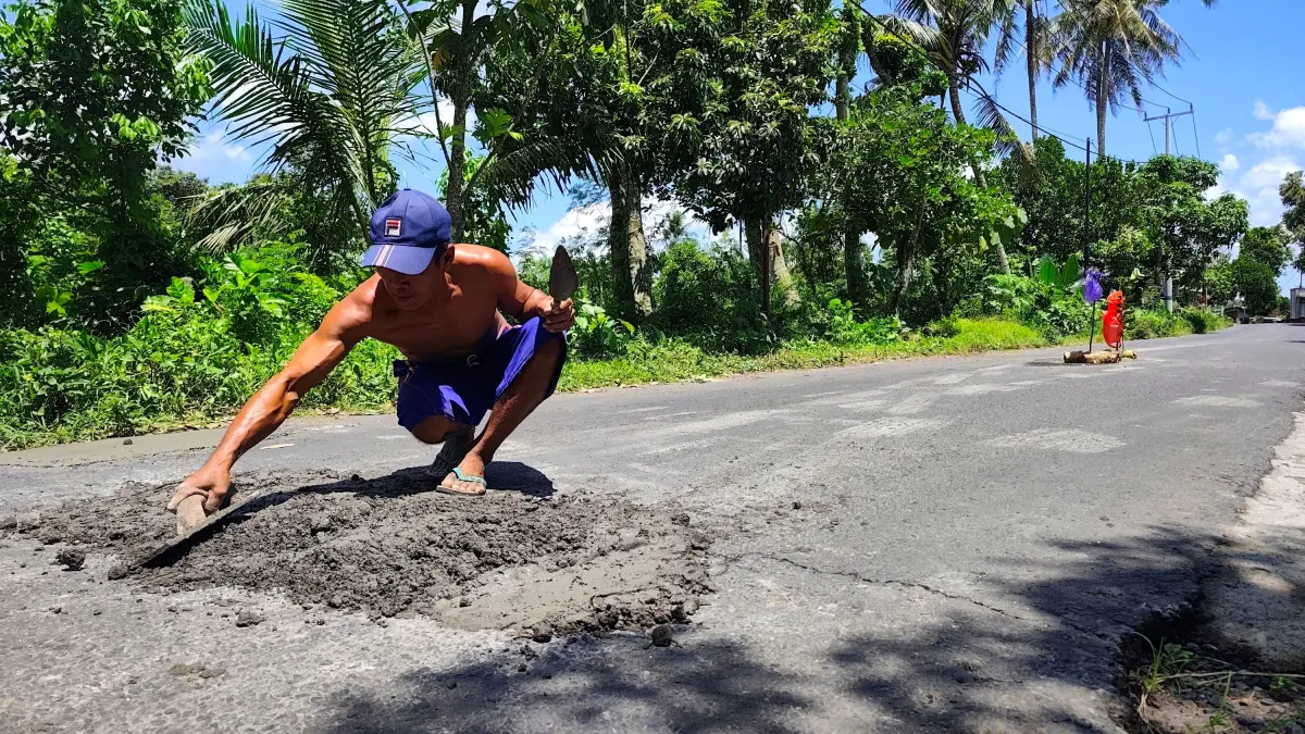 Seorang warga menambal jalan berlubang menggunakan adonan semen swadaya Masyarakat di Desa Pringgarata, Pringgarata, Loteng, beberapa waktu lalu.
