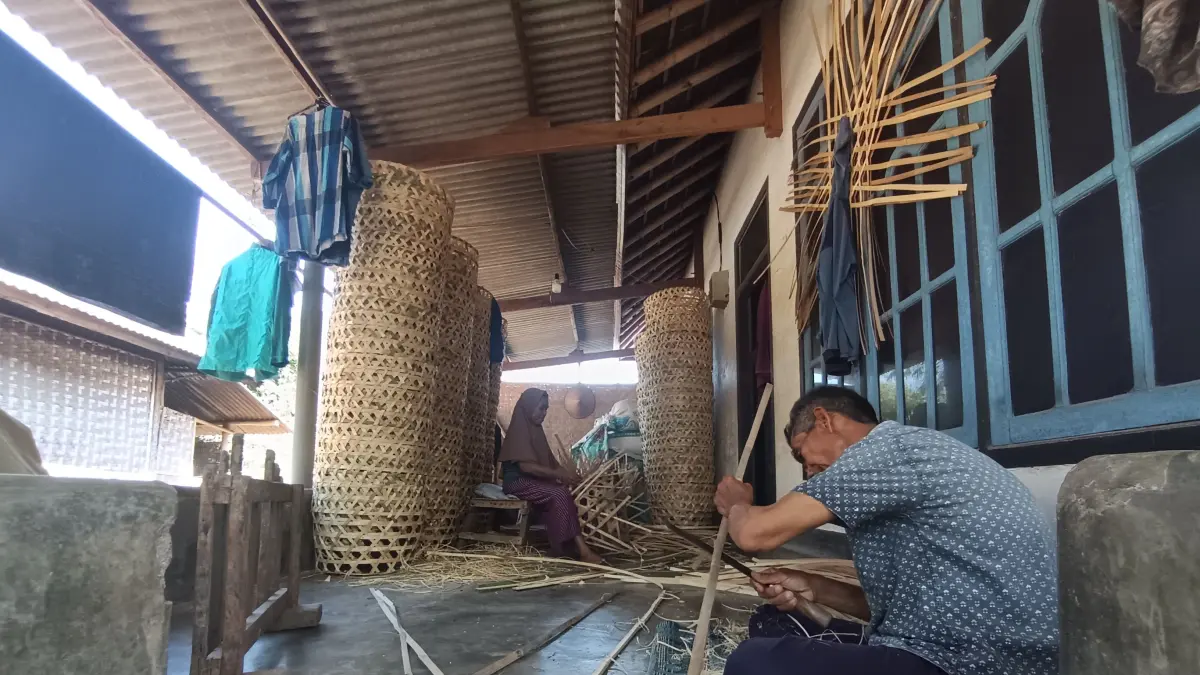 ANYAMAN BAMBU: Nursihan sedang fokus membuat keranjang bambu di teras rumahnya bersama suaminya.