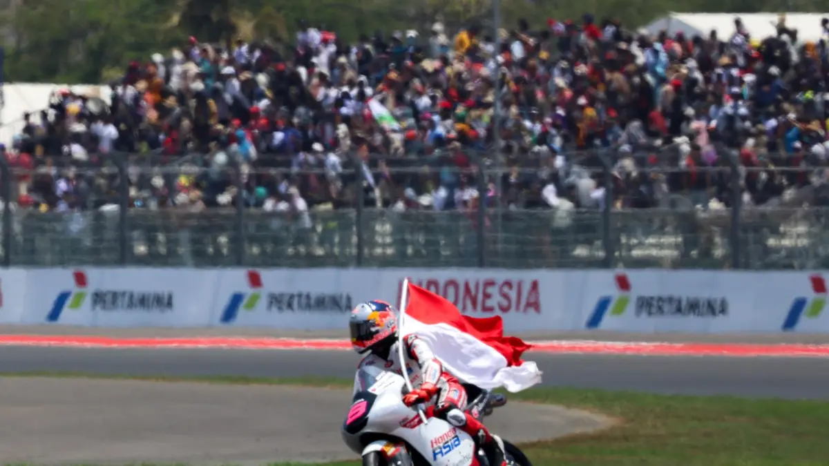 PECAHKAN REKOR: Pembalap Moto3 asal Indonesia Veda Ega Pratama membawa Bendera Merah Putih dengan latar ribuan penonton yang memadati salah satu tribun saat MotoGP Mandalika 2026 di Sirkuit Internasional Mandalika, Lombok Tengah, Ahad (11/10). (Ivan/Lombok Post)