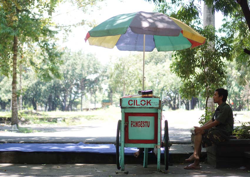 MENUNGGU PEMBELI: Seorang pedagang cilok sedang duduk menunggu pembeli sambil memandang eks Taman Rinjani Selong yang gagal jadi Taman Sadir Square, kemarin (15/2).