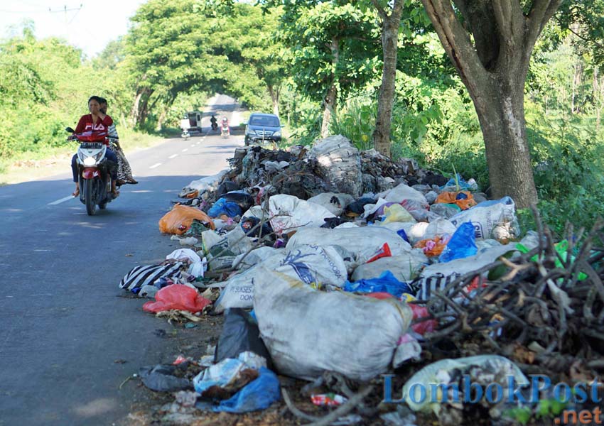 TUTUP HIDUNG: Seorang pengendara menutup hidung saat melintas di depan tumpukan sampah di pinggir jalan perbatasan Desa Ketapang Raya, Kecamatan Keruak, belum lama ini.