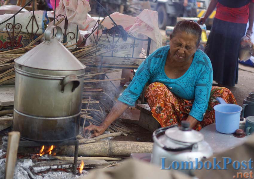 JURU MASAK: Inaq Sukardi, korban gempa dari Dusun Solong, Desa Pesanggrahan, Kecamatan Montong Gading sedang membesarkan api tungkunya di dapur umum pengungsian, kemarin (21/3).