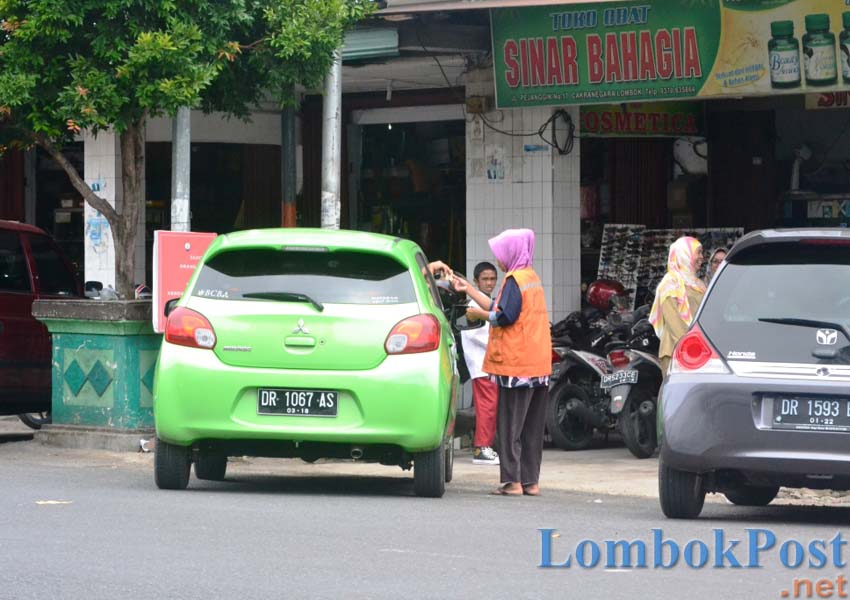 LINCAH: Seorang jukir perempuan tengah menerima pembayaran dari parkir mobil di lahan tempat ia menjaga parkir di Kawasan Bisnis Cakranegara, Kota Mataram, Kamis (7/3).