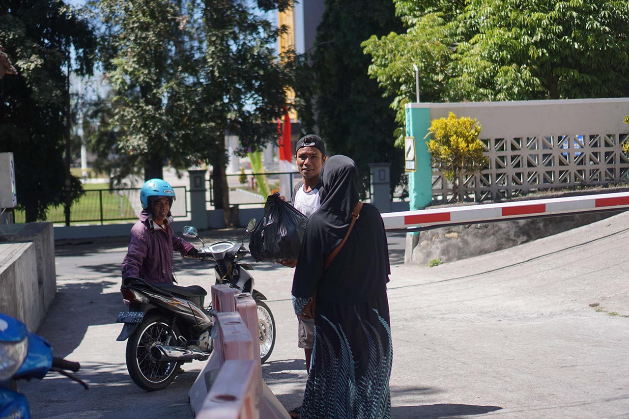 DEKAT DENGAN WARGA: Seorang jukir RSUD Selong terlihat sedang membantu seorang pengunjung mengangkat barang bawaannya di area parkir, belum lama ini.