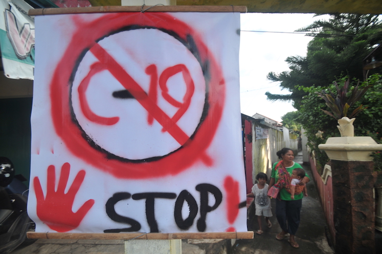 LOCKDOWN LOKAL: Warga melintas di dekat spanduk larangan bagi penderita Korona di salah satu desa Purworejo, Jawa Tengah, kemarin (31/3). Kini, banyak desa yang memberlakukan lockdown secara lokal untuk meminimalisir penyebaran Korona (Anwar Mustafa/AFP)