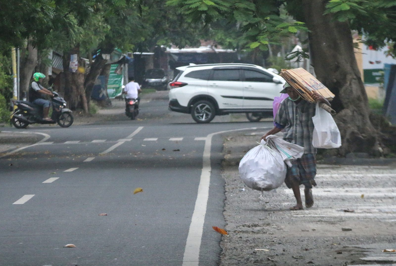 PANTAS DIBANTU: Seorang pemulung membawa kardus dan botol plastik di jalanan Kota Mataram, kemarin.