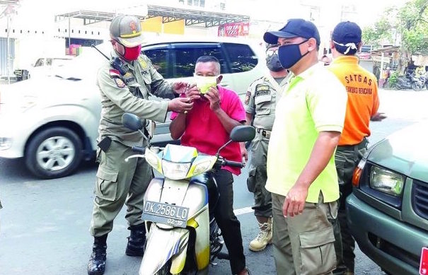 AKSI SIMPATIK: Anggota Satpol PP NTB memasangkan masker kepada pengguna jalan yang tidak pakai masker, (8/5) lalu.