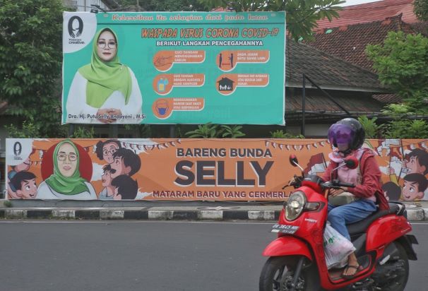 SOSIALISASI: Seorang pengendara melintas di depan mural dan baliho milik bakal calon Wali Kota Mataram. (IVAN/LOMBOK POST)