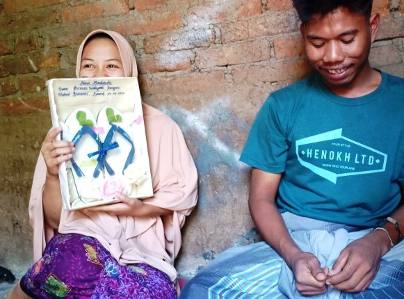 MALU-MALU: Helmi Susanti, memegang bingkai berisikan sandal jepit yang merupakan pernikahannya dengan Iwan Firman Wahyudi di Sendong Sekeq Desa Beraim, Praya Tengah, Lombok Tengah, Sabtu (4/7) (Dedi/Lombok Post)