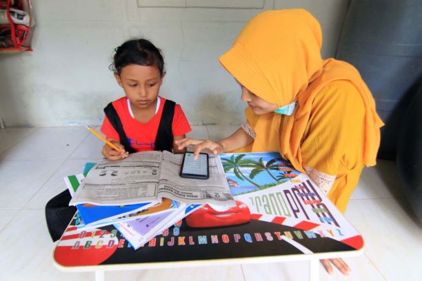 MEMILIH PATUH: Fatma, membimbing anaknya Najwa yang baru kelas I sekolah dasar dengan materi yang disiapkan guru dan dikirim melalui telepon genggam. Tahun ajaran baru telah dimulai para siswa di NTB masih tetap menjalani belajar dari rumah. (JPG)