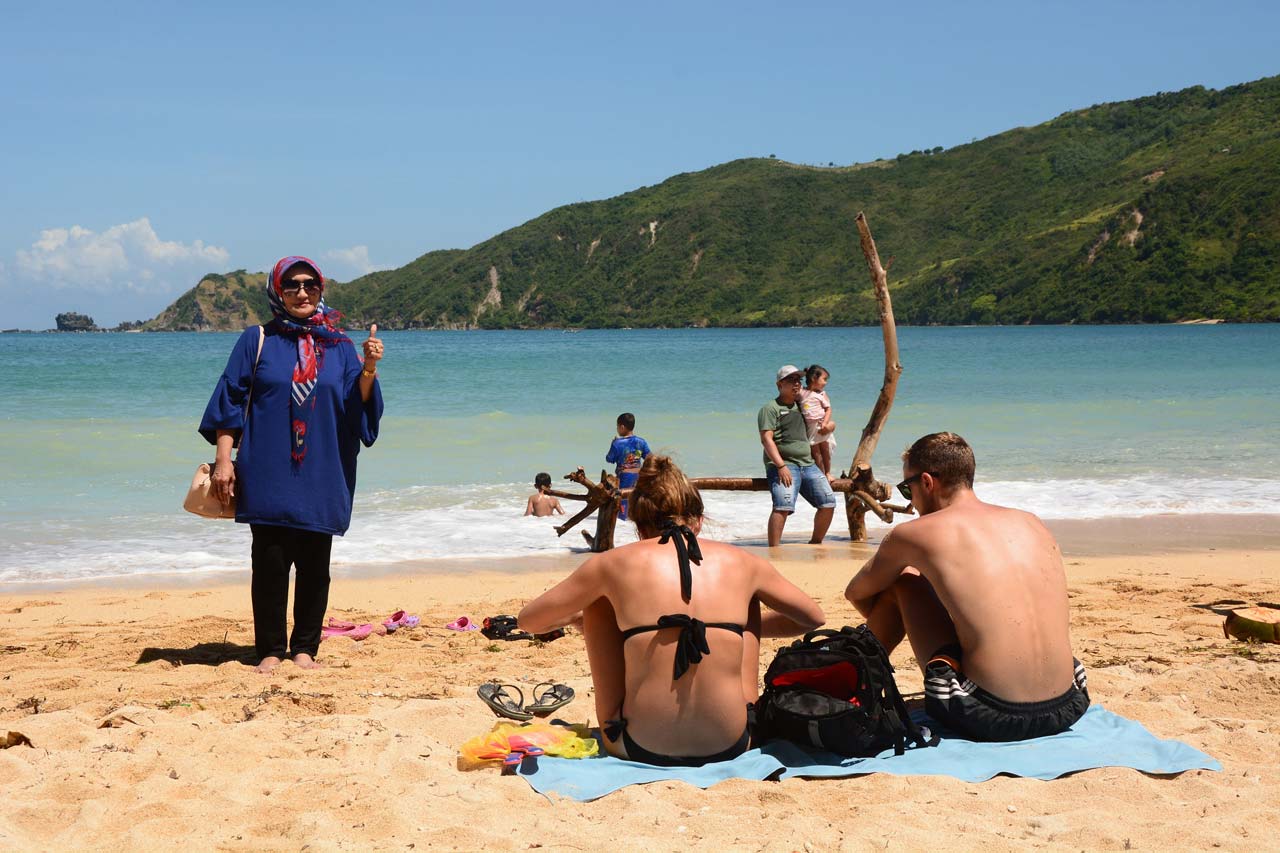 WISATA HALAL: Seorang wisatawan lokal berpose dengan latar belakang Pantai Kuta, KEK Mandalika, Lombok Tengah. Sementara dua turis asing menikmati keindahan pantai dengan berjemur.