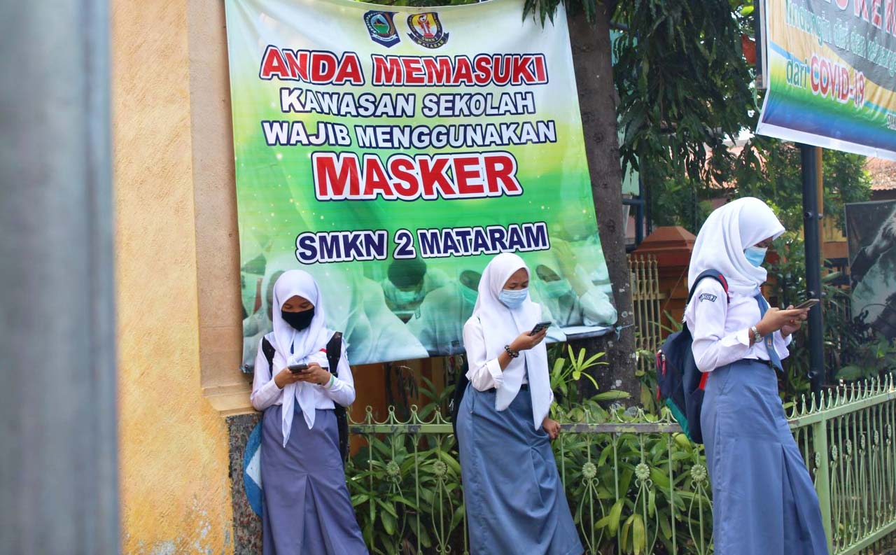 SIBUK SENDIRI: Tiga siswa SMKN 2 Mataram memainkan ponsel pintarnya masing-masing, sambil menunggu dijemput orang tua, usai melaksanakan simulasi KBM tatap muka, September lalu.
