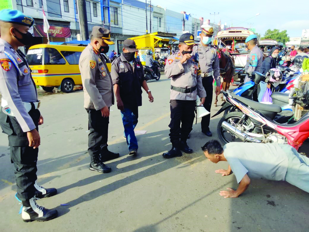 PATUT DIHUKUM: Kapolresta Mataram Kombes Pol Heri Wahyudi (dua dari kiri) menghukum seorang juru parkir di Pasar Kebon Roek, Ampenan, yang tidak menggunakan masker, Selasa (12/1).   (harli/lombok post)
