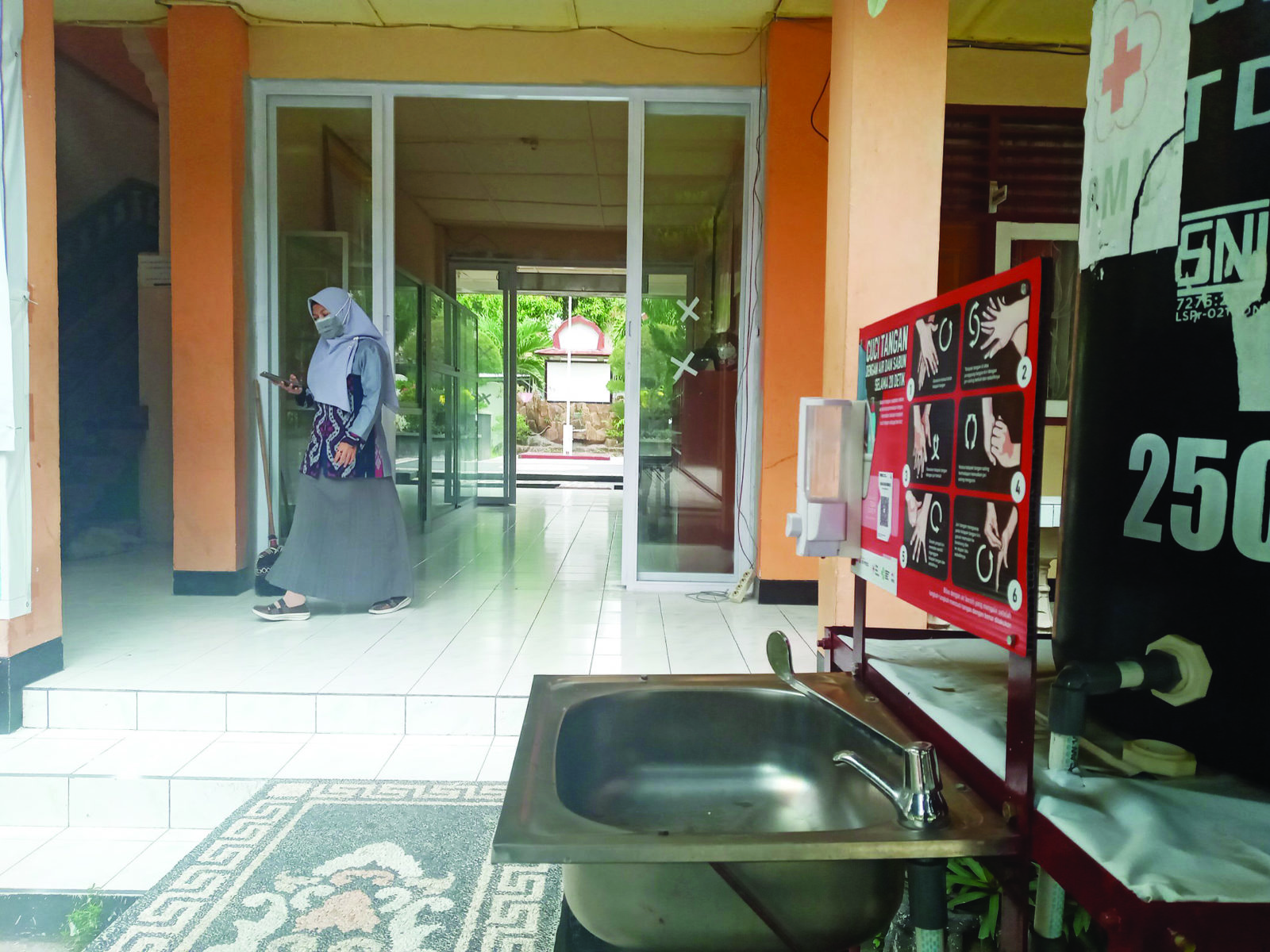 TERAPKAN PROKES YA: Seorang guru melintas melalui pintu masuk utama di SMPN 9 Mataram, pekan lalu. Dalam PTM semua sekolah wajib menerapkan prokes. (rojai/lombok post)