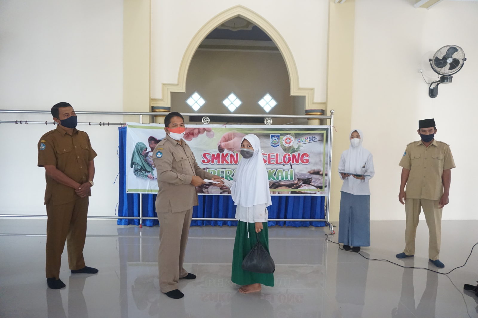 BERSEDEKAH: Kepala SMKN 2 Selong Hasbi Ahmad (kiri) secara simbolis menyerahkan sedekah kepada anak yatim di Masjid Dusun Lendang Batu, Desa Sukamulia Timur, Kecamatan Sukamulia, Senin (1/2). (Supardi/Lombok Post)