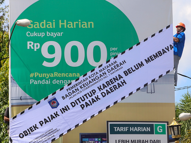 BAYAR PAJAK DULU: Seorang pekerja memasang spanduk tanda belum bayar pajak di papan reklame di Jalan Pejanggik, Kelurahan Cilinaya, Cakranegara, Kota Mataram, Kamis (1/7) lalu. (Ivan/Lombok Post)