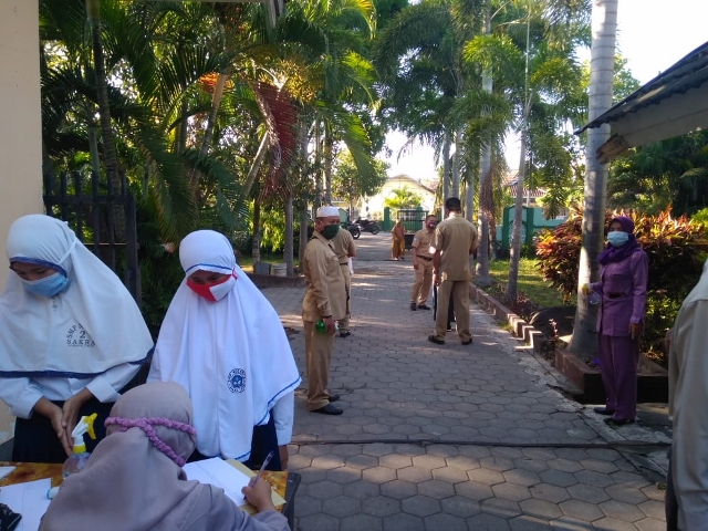 TAAT PROKES: Guru SMPN 2 Sakra melakukan pemeriksaan terhadap siswa yang baru datang di sekolah, belum lama ini. (Fatih/Lombok Post)