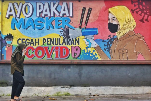 MAKANYA PAKAI MASKER: Seorang warga melintasi depan mural Covid-19 sambil bersin di Karang Medain, Kota Mataram, belum lama ini.( DOK/LOMBOK POST)