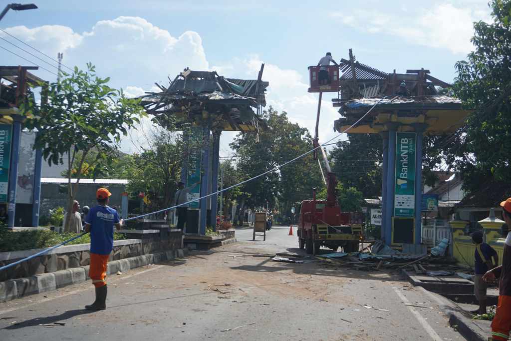 DIROBOHKAN: Petugas kebersihan DLH Lotim sedang merobohkan atap gapura di Kelurahan Pancor, Kecamatan Selong, Minggu (14/8). (Fatih/Lombok Post)
