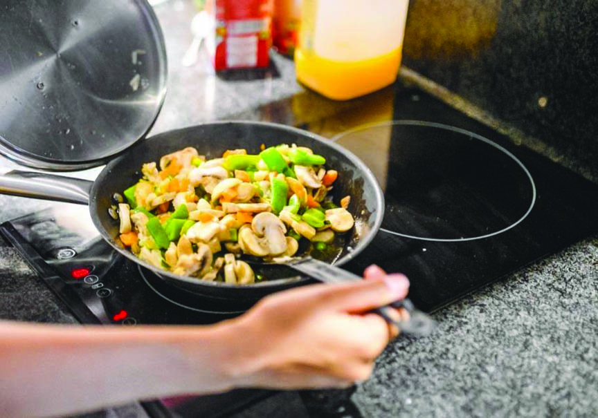BATAL: Seorang warga memasak menggunakan kompor listrik. Untuk menjaga kenyamanan masyarakat di masa pemulihan ekonomi pascapandemi Covid-19, PLN membatalkan program pengalihan kompor gas ke kompor listrik. (Foto: Istimewa)