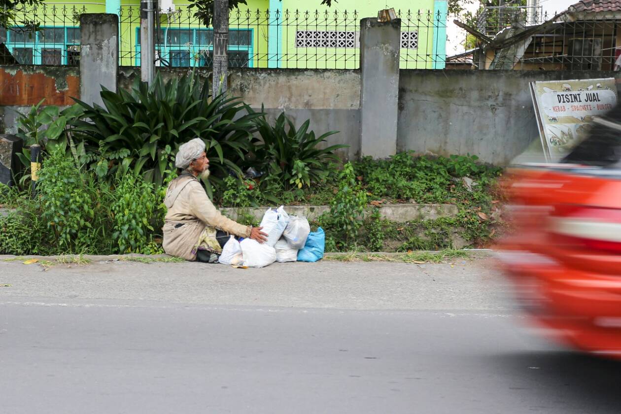 TARGET NOL: Seorang tunawisma duduk ditepian selokan pinggir jalan menunggu belas kasihan pengendara yang melintas di Kota Mataram, belum lama ini. (Ivan/Lombok Post)