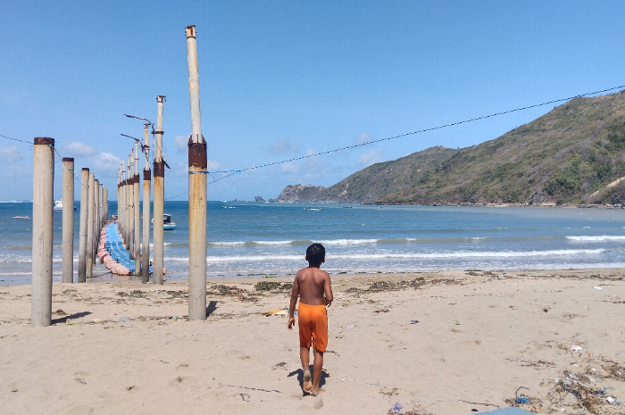 MENGURUS IZIN PUSAT: Seorang anak melintas di depan dermaga apung Pantai Kuta, Desa Kuta, Kecamatan Pujut, Loteng, Selasa (11/7). Pengurusan ijin pembangunan pelabuhan kapal cepat masih ditangani pemerintah pusat. (Dewi/Lombok Post)
