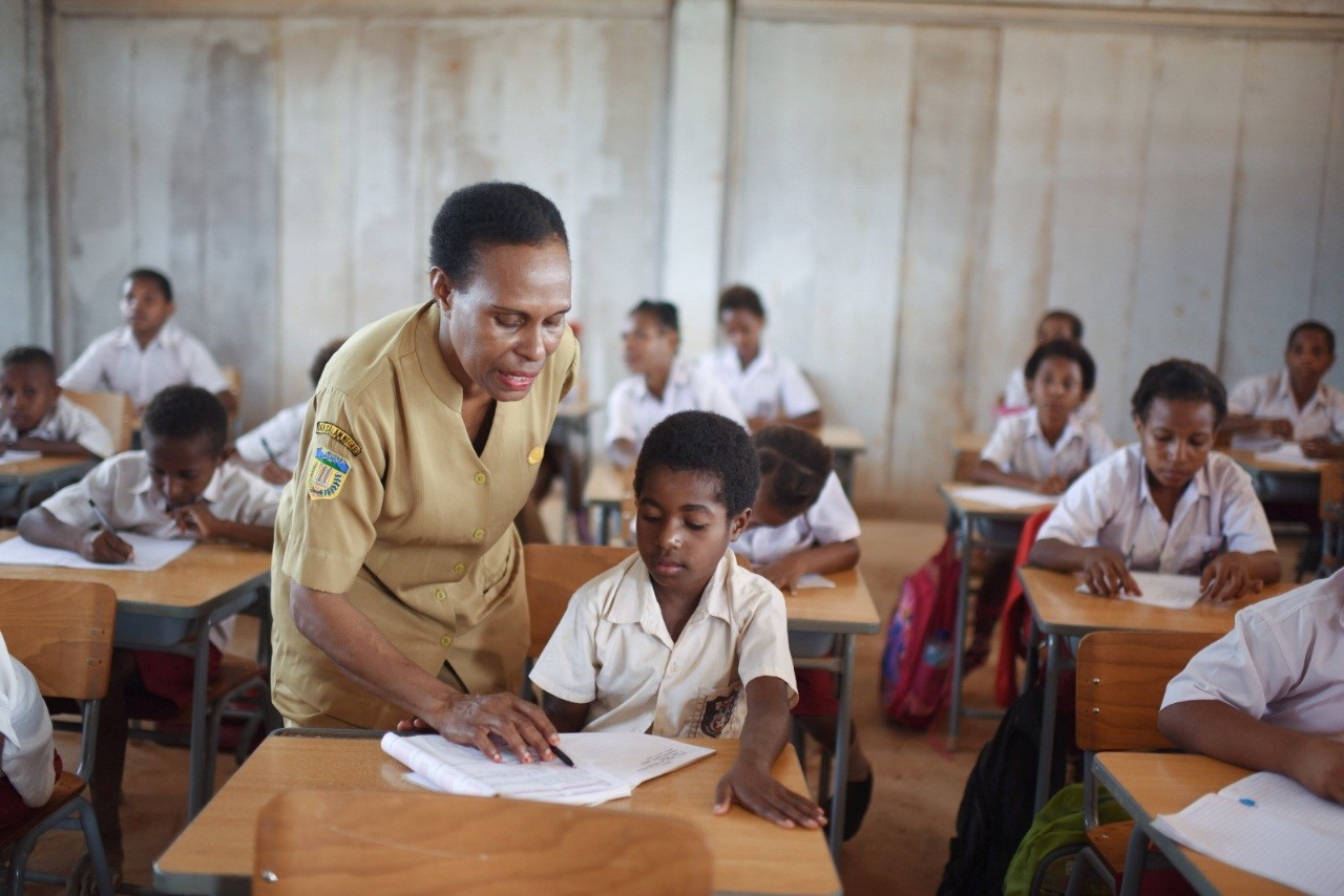 Seorang guru sekolah dasar di Papua dengan penuh kesabaran sedang mengajar murid laki-lakinya