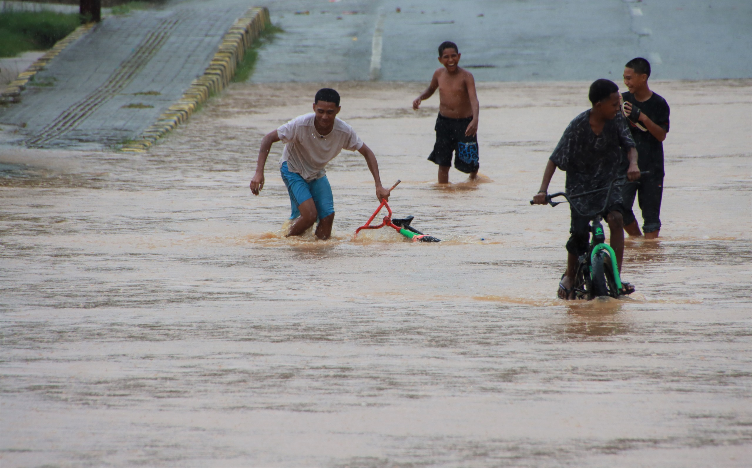 Lokasi ruas jalan depan Koramil Japsel kerap tergenang air disaat intensitas hujan tinggi. Nampak empat anak tengah bermain di tengah genangan air pada banjir di ruas jalan tersebut, Sabtu (1/11/2025)