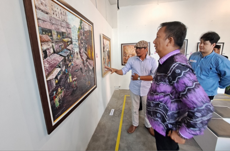 BERAGAM: Muslim Anang Abdullah (bertopi) menjelaskan lukisannya kepada Kepala Bidang Kebudayaan di Disbudporapar Banjarmasin, Zulfaisal Putera.