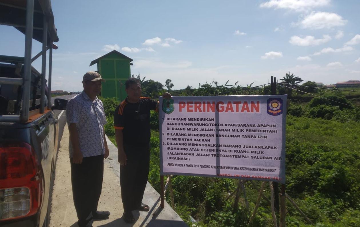 TEGAS:Anggota Dinas Pol PP dan Damkar HSU memasang spanduk peringatan dilarang berjualan di Jalan Bypass Bayur-Panangkalaan, Rabu (5/6/2024).(Foto:M Akbar/Radar Banjarmasin)