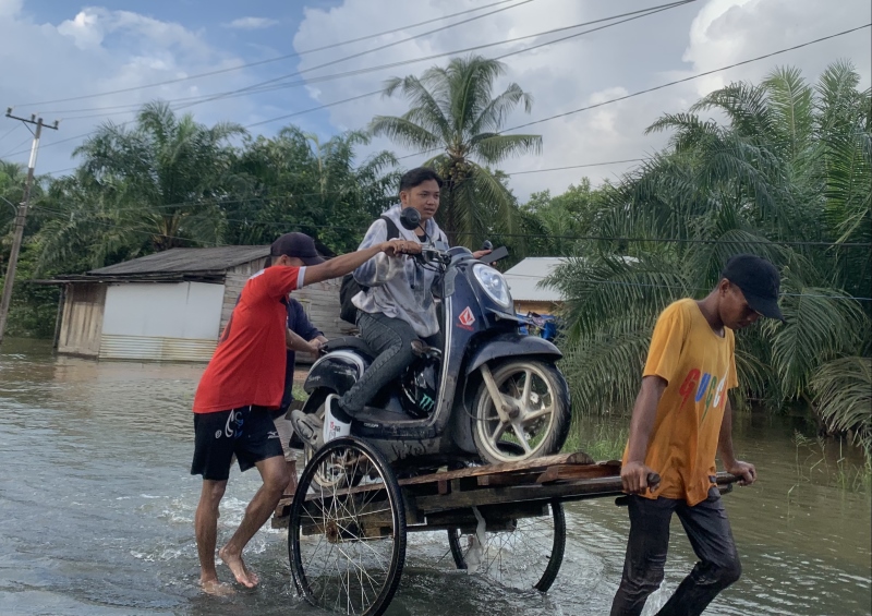NAIK GEROBAK: Warga membantu pesepeda motor menyeberangi Jalan Valgoson, Kusan Hulu, Tanah Bumbu yang terendam, Senin (10/6).