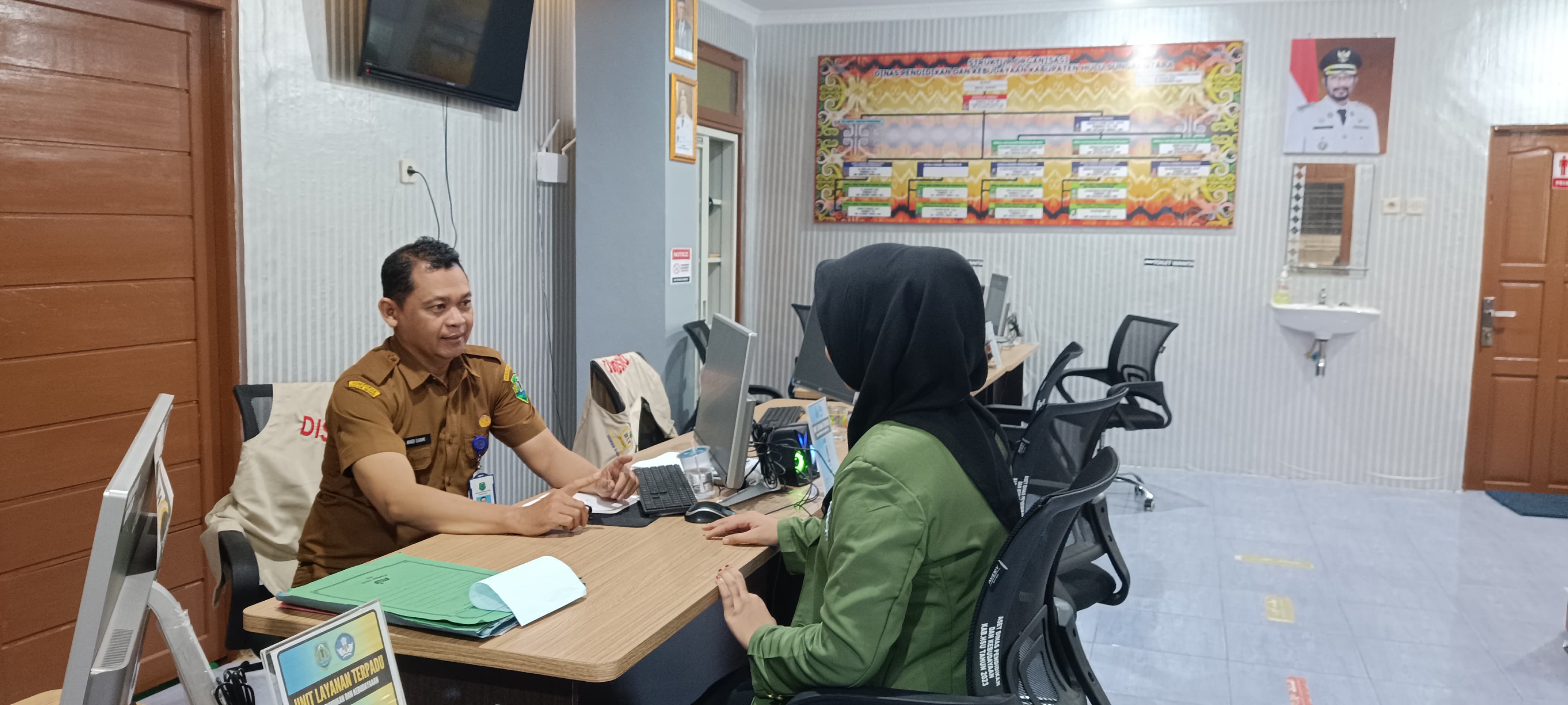 LAYANAN: Sekretaris Disdikbud HSU Ahadi Ilhani melayani seorang mahasiswa yang memerlukan data di ULT Disdibud HSU, Rabu (10/7). (Foto: M.Akbar/Radar Banjarmasin)