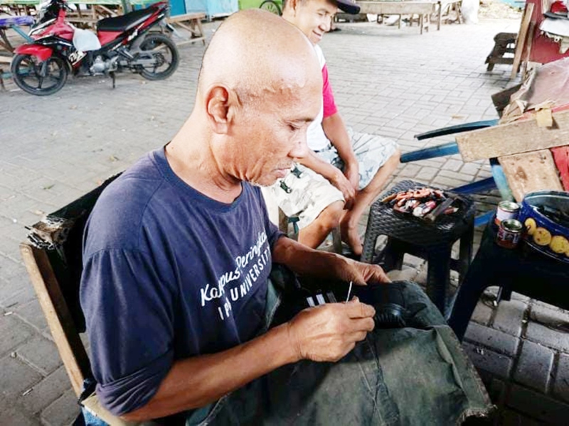 MENJAHIT: Rahmadi sedang sibuk menjahit sepatu yang rusak di lapaknya, Jumat (19/7).