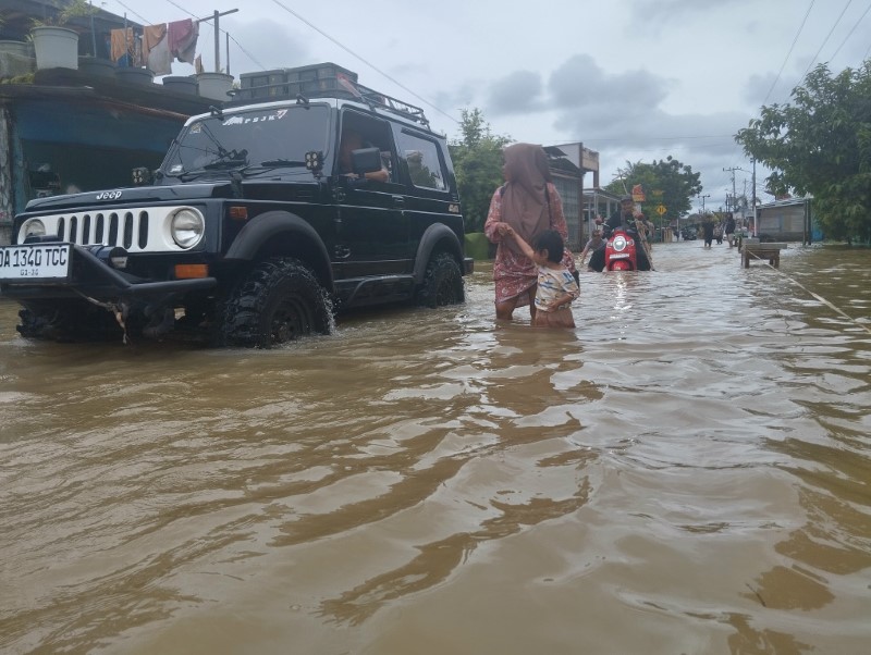 TERENDAM: Ibu menuntun anaknya saat melintasi banjir di Desa Pekauman, Kecamatan Martapura Timur, Kabupaten Banjar