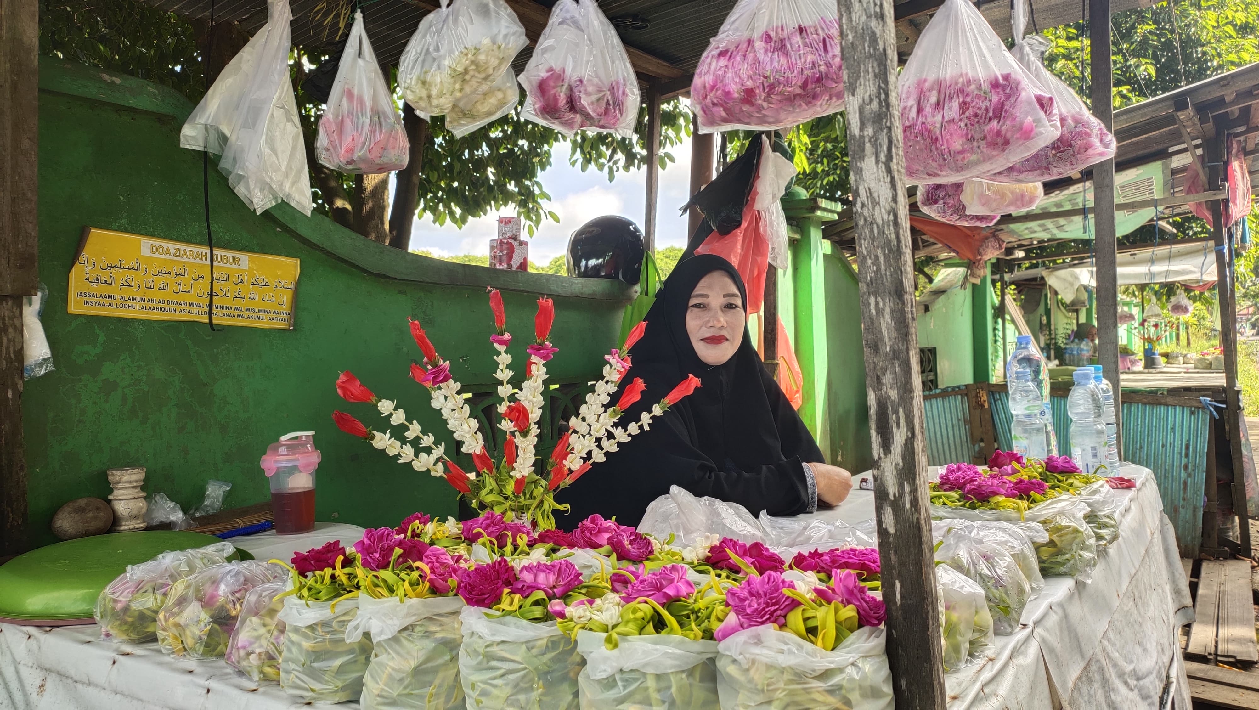 JAGA LAPAK: Saniah (50) sedang menjaga lapak jualan bunga taburnya di samping gapura Kuburan Muslimin Guntung Lua, Kemuning, Rabu (16/4) pagi.